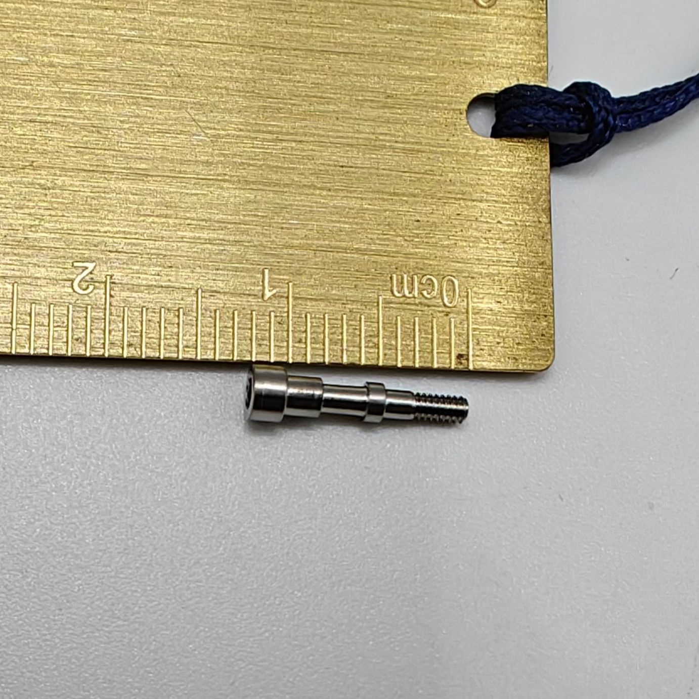 Two small metal objects next to a gold ruler on a gray background