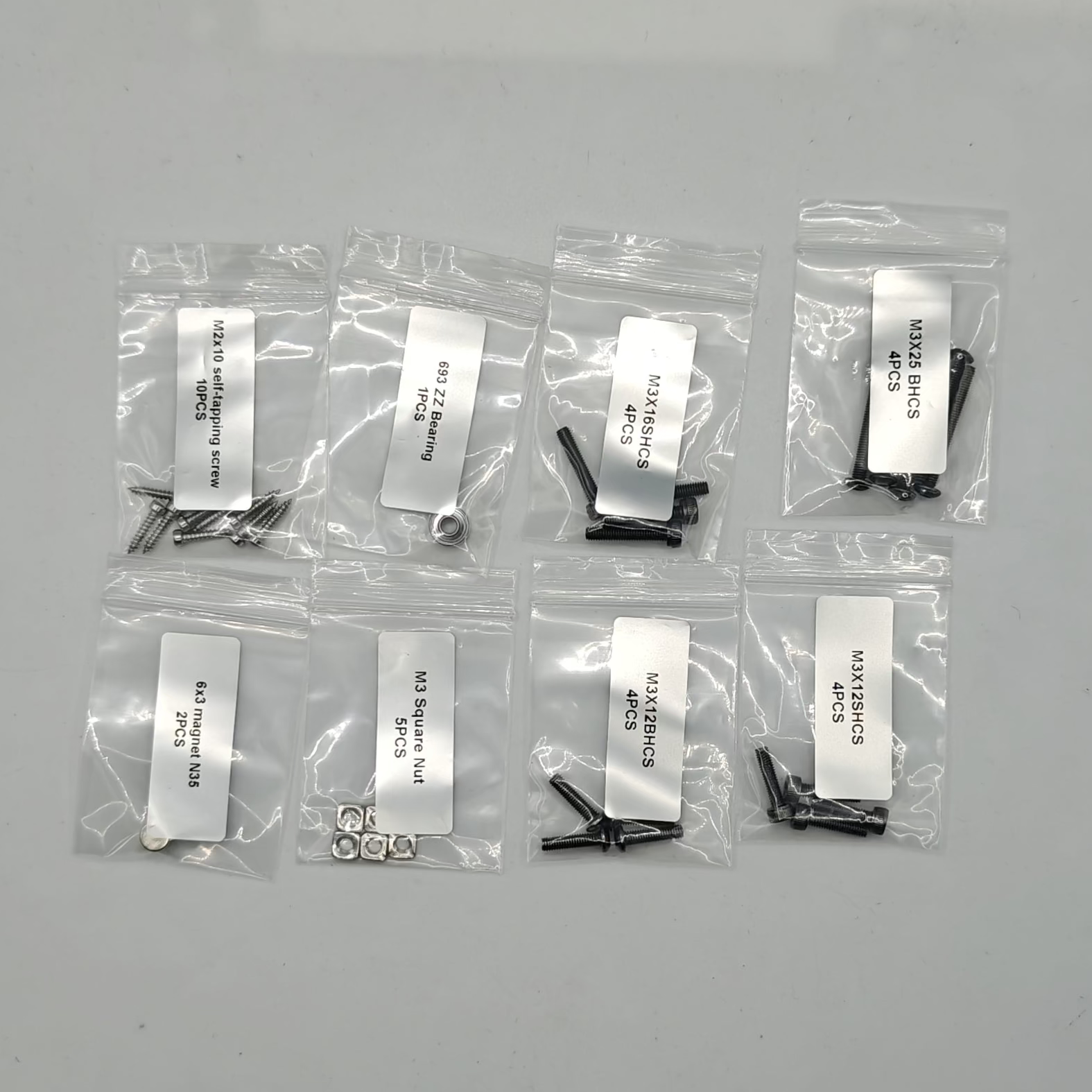 Set of small mechanical parts in clear plastic bags with labels on a gray background