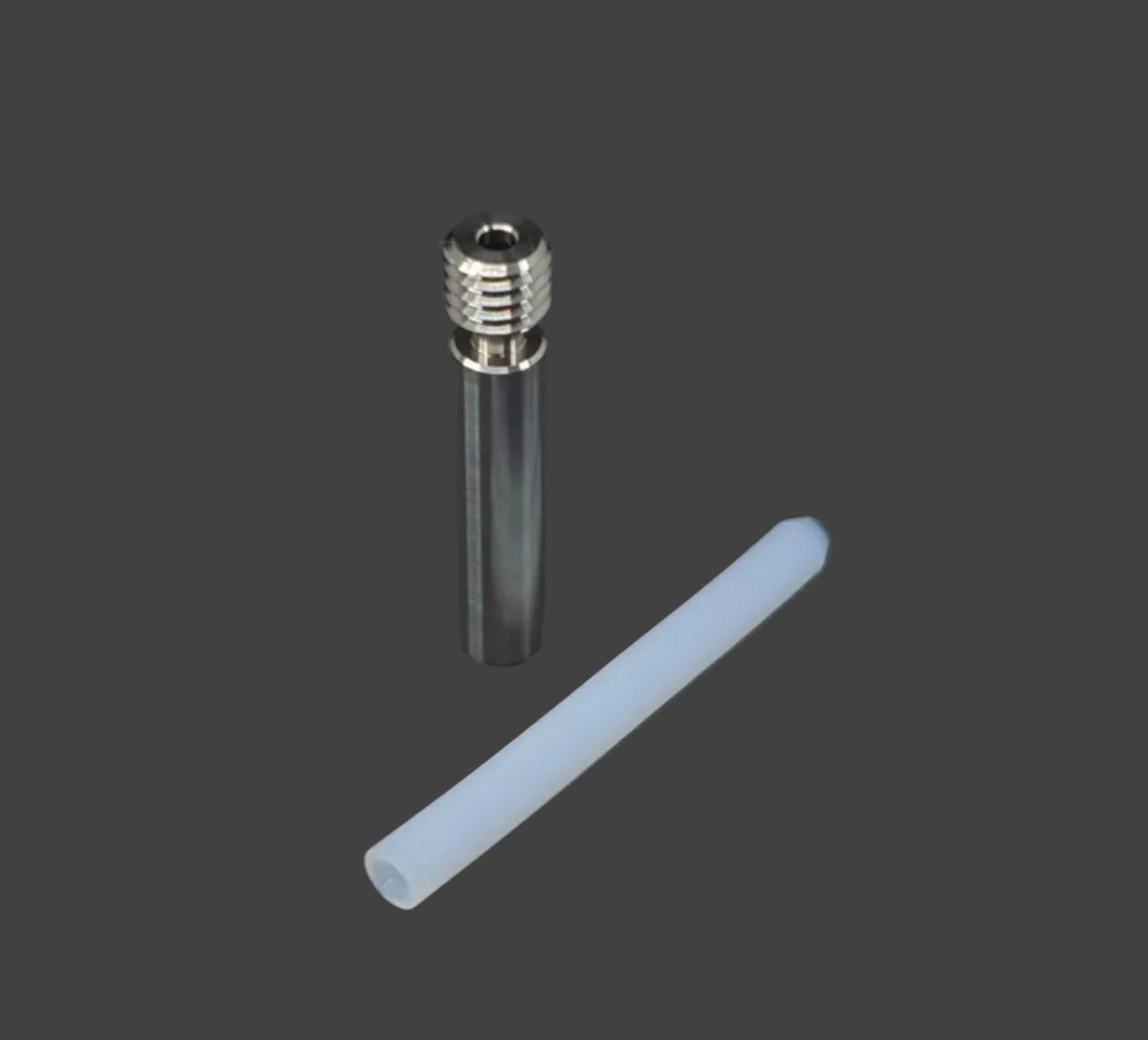 A small metal cylindrical component with a threaded top next to a translucent white plastic tube, photographed on a dark gray textured background.