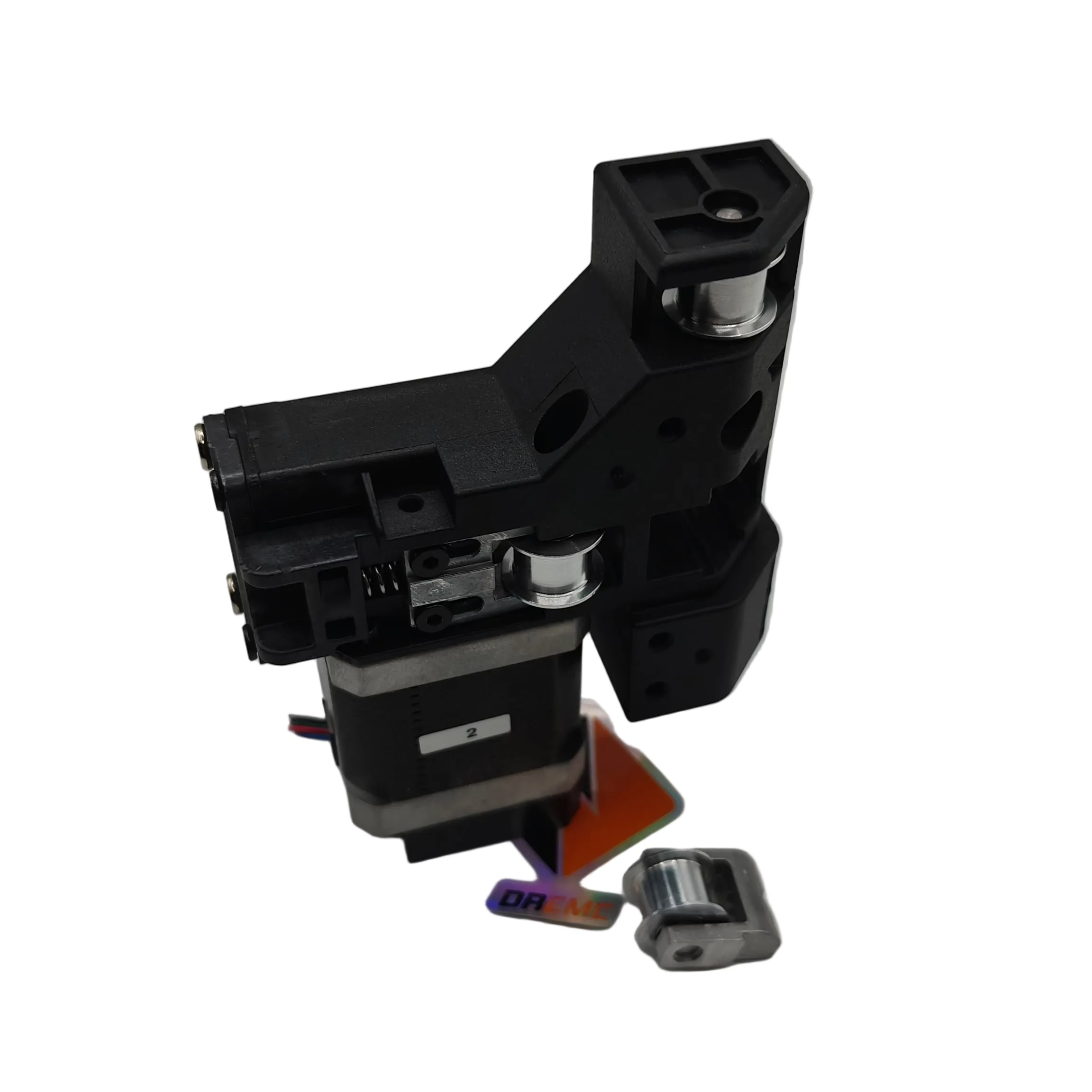 A black and silver mechanical component, likely a linear actuator or motor assembly, shown on a neutral gray background with a small orange piece and a small metal part placed in front of it.
