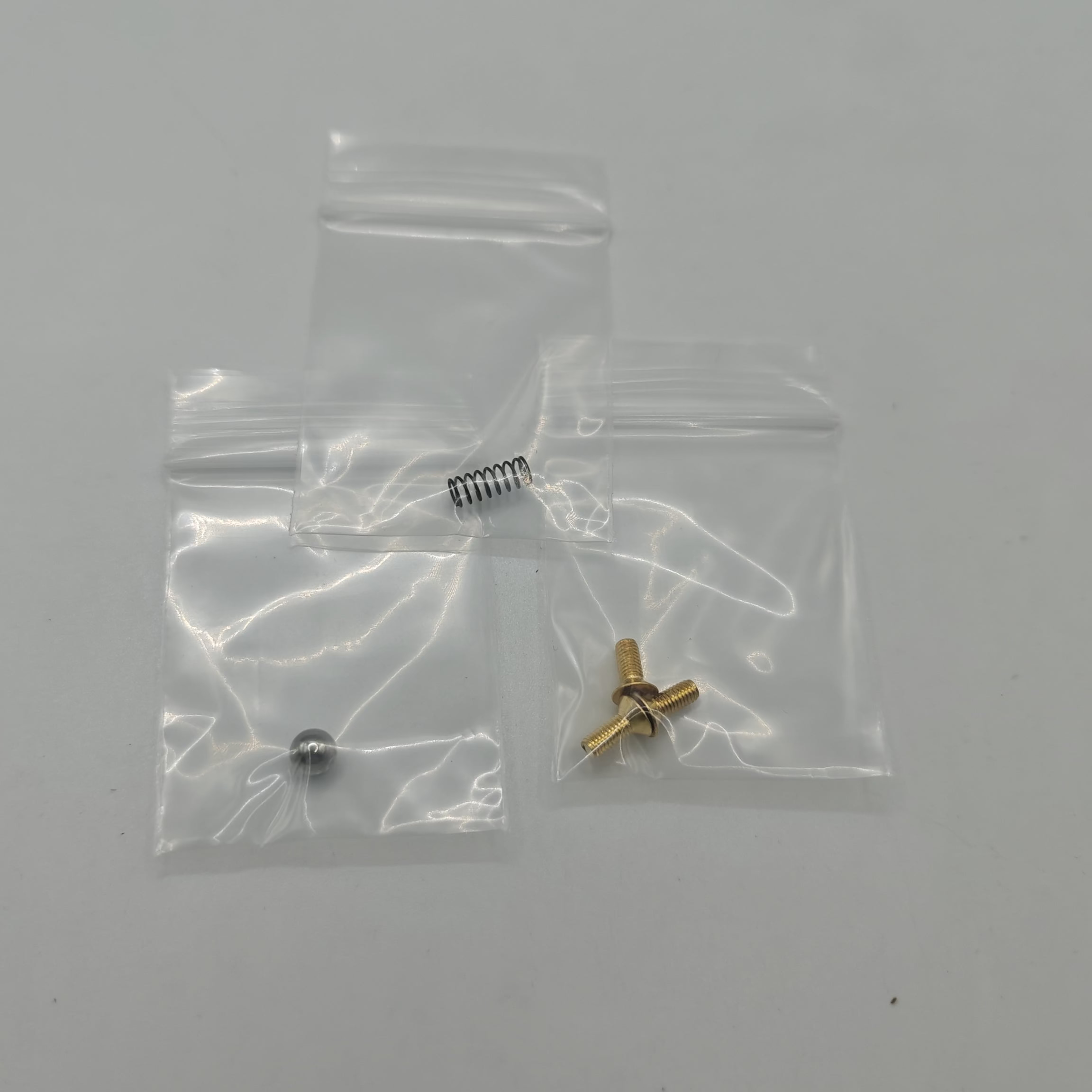Two small metal components in clear plastic bags on a white background