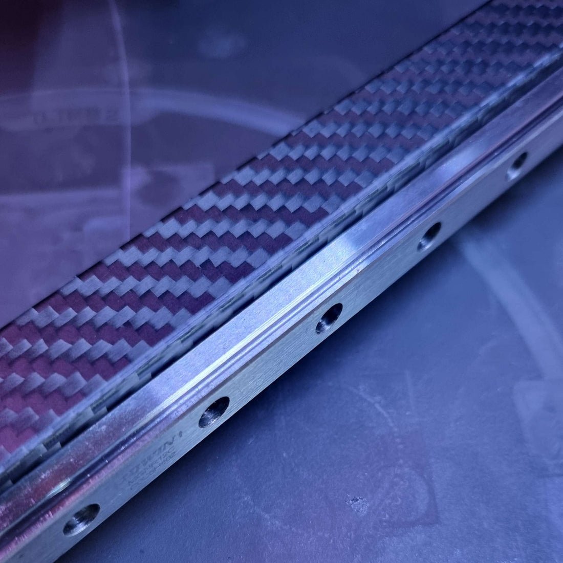 Close-up of a metal slide rail with carbon fiber pattern on a blurred background