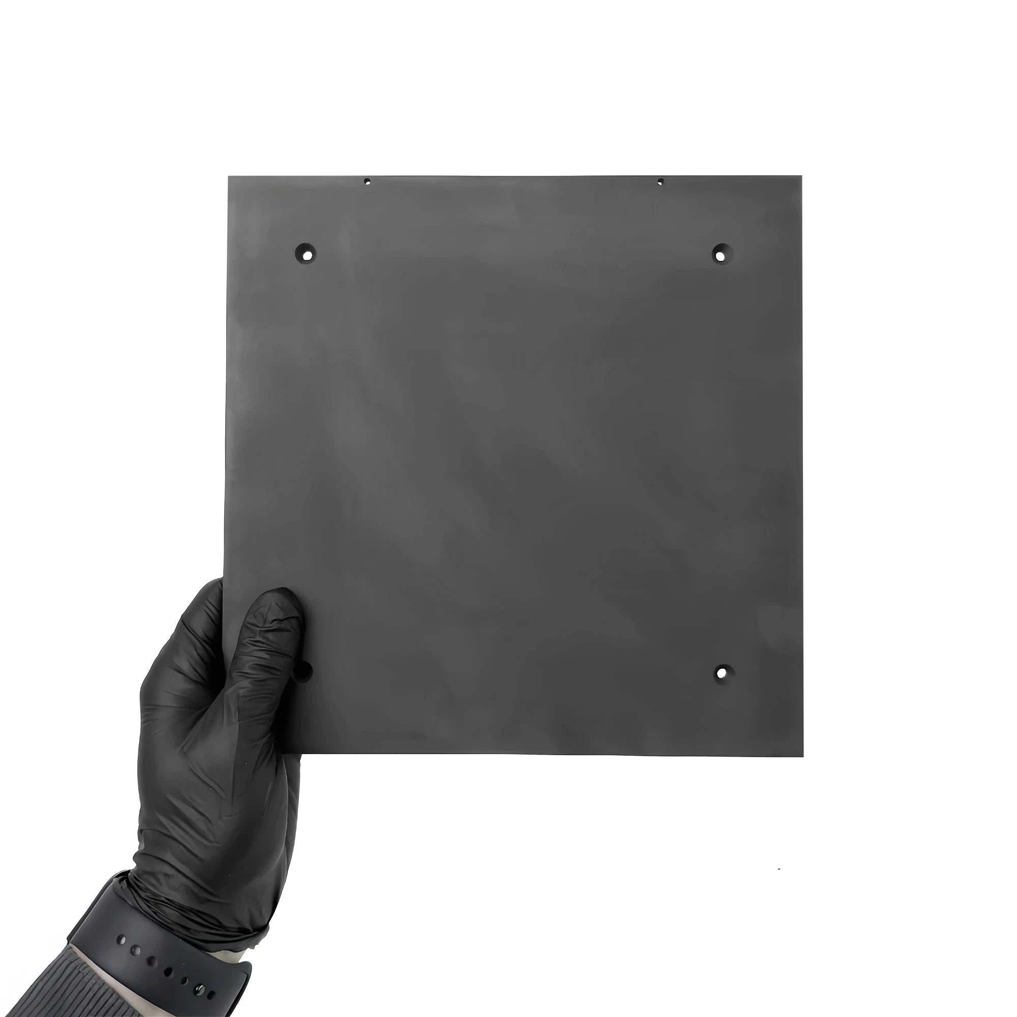 A hand wearing a black glove holding a square graphite plate with two holes for mounting.