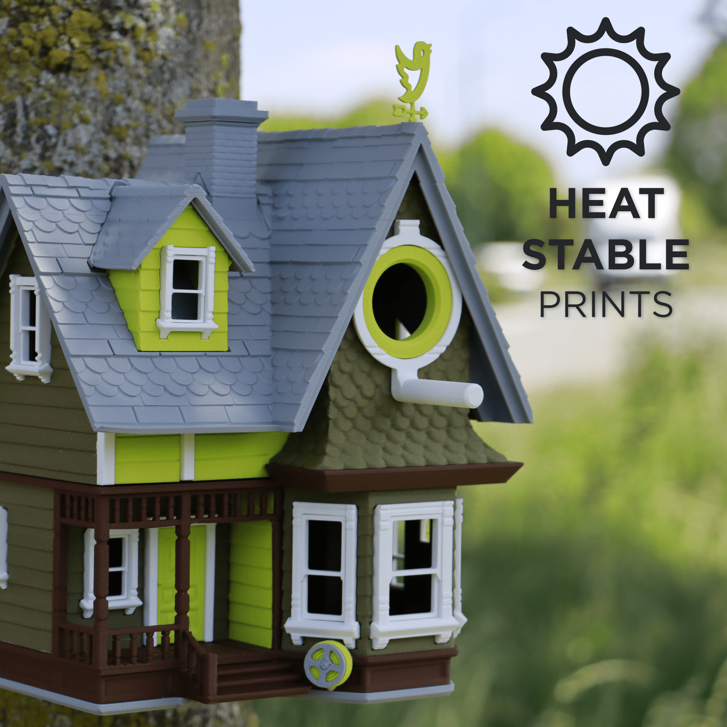 Model house with green and brown colors on a blurred natural background, featuring 'Heat Stable Prints' text.