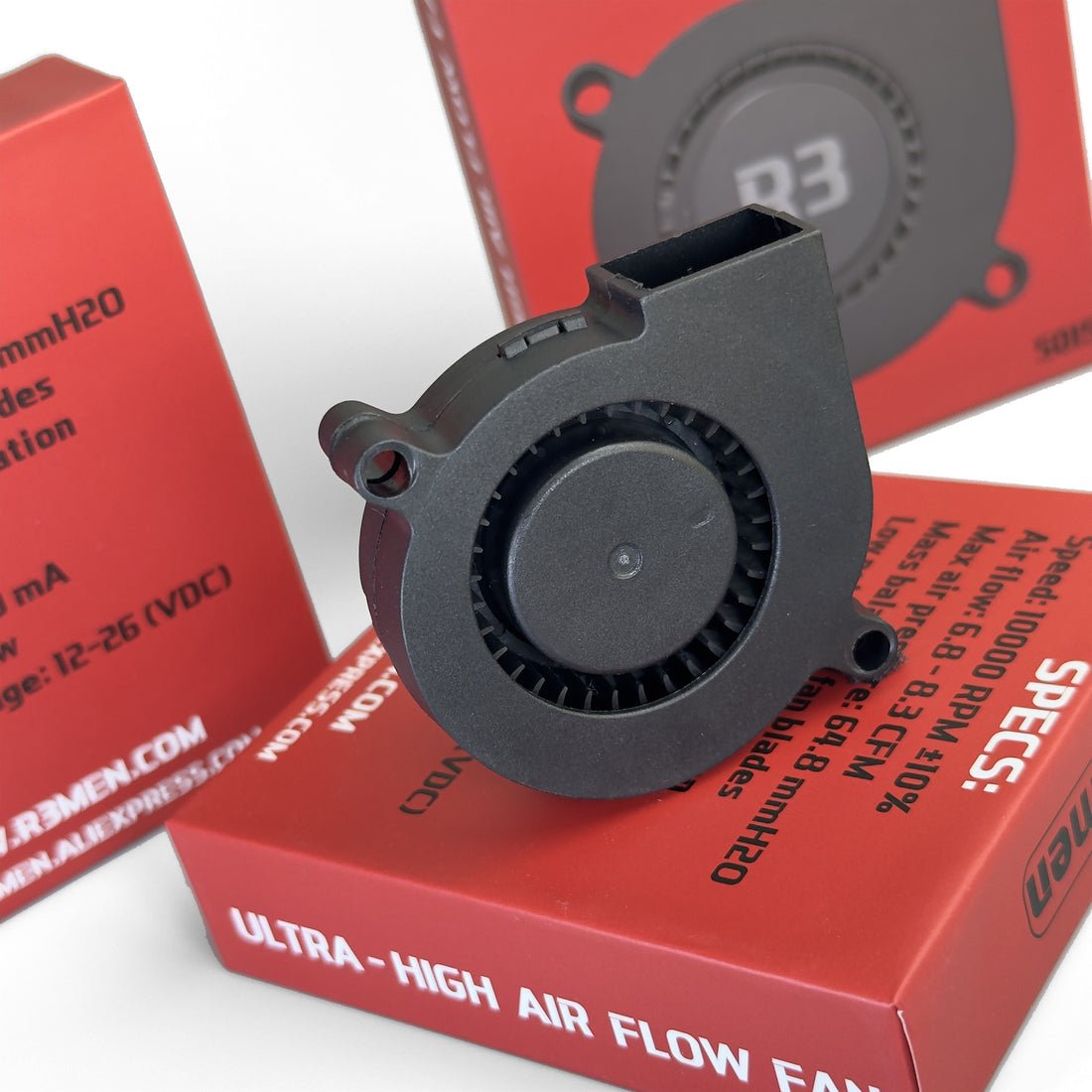 A black high-flow centrifugal cooling fan placed on top of red branded product boxes. The fan is shown in close-up with the back grille visible, and the packaging includes printed specs and the brand name R3MEN.